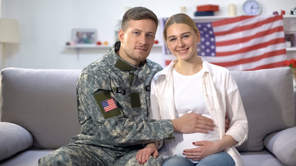 Man in military uniform stroking belly of pregnant wife, american nation concept