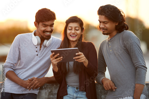 Cheerful young Indian friends playing in digital tablet Canvas Print