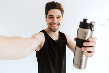 Wall Mural - Smiling young strong sports man posing isolated over white wall background drinking water take a selfie by camera.