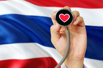 Doctor holding stethoscope with red love heart. National Thailand flag background. Healthcare system concept, medical theme.