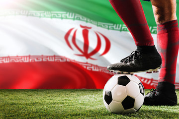 Close up legs of Iran football team player in red socks, shoes on soccer ball at the free kick or penalty spot playing on grass.