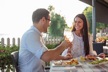 Beautiful happy young couple making a toast, celebrating anniversary or birthday in a restaurant. Husband and wife having romantic dinner in a restaurant by the river