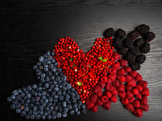 Heart of berries on a wooden background. Red raspberries, cranberry, blueberry, blackberry. Tasty, vitamin food