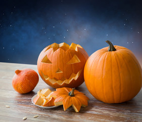 halloween, holidays and decoration concept - jack-o-lantern or carved pumpkin on wooden table over starry night sky background