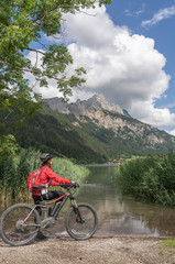 Wall Mural - nice and active senior woman, riding her e-mountain bike in the Tannheim valley along side the Haldensee, Tirol, Austria, with the village of Tannheim and famous summits Gimpel and Rote Flueh