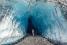 A Woman Walking Into An Ice Cave In Alaska 