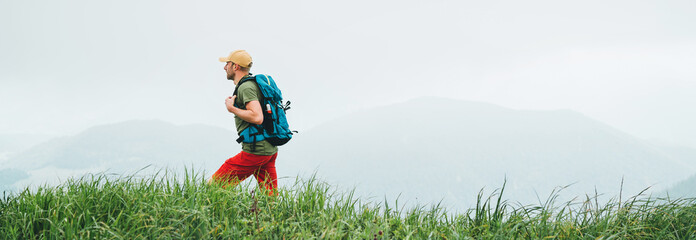 Wall Mural - side shot of hiker man walking by the foggy cloudy weather mountain range path with backpack. active