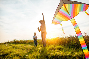 Father with son launching colorful air kite on the field during the sunset. Concept of a happy family having fun during the summer activity