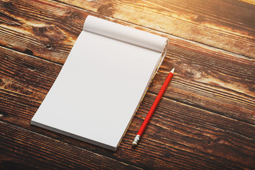 Wall Mural - Notebook with a red pencil on a brown background with warm sunlight, for writing. Free empty space for writing on a blank sheet of a notebook.