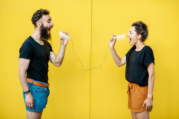 Man and woman talking with string phone, shouting on each other on the yellow background. Concept of communication and misunderstanding