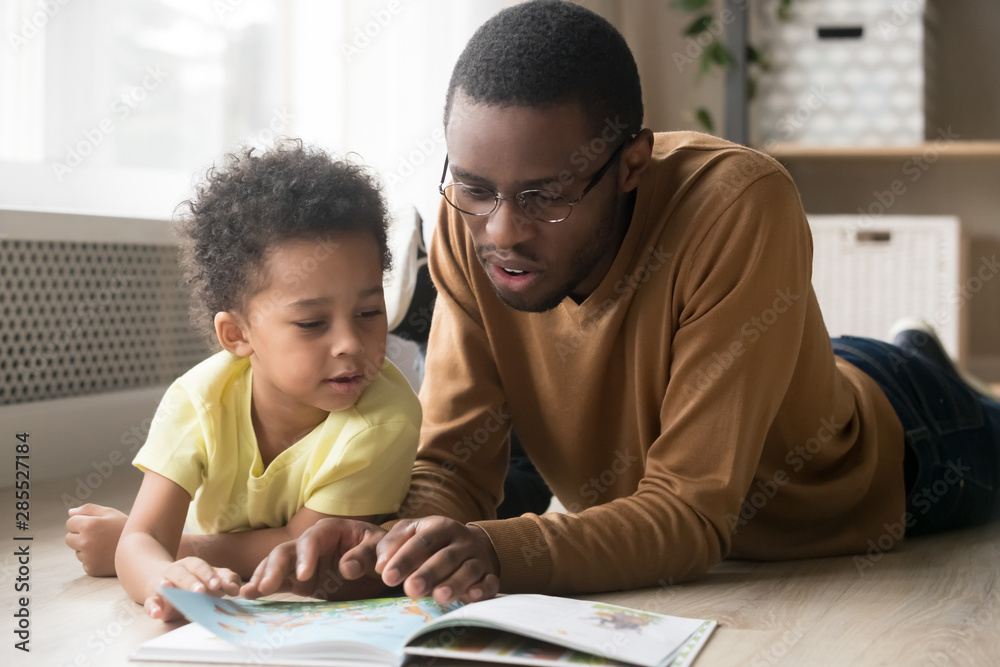 African American father and toddler son reading book together - obrazy, fototapety, plakaty 