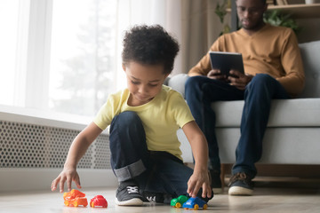 Wall Mural - Preschooler son playing with toys while African American father working