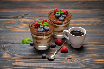 Classic tiramisu dessert with blueberries and strawberries in a glass cup and espresso coffee on wooden background