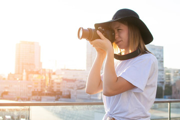 Canvas Print - portrait of a girl photographer, a woman with a modern camera photographs against the backdrop of a city sunset