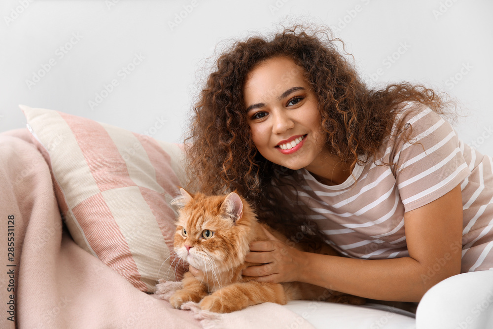 Young African-American woman with cute cat at home - obrazy, fototapety, plakaty 