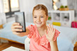© Syda Productions - people, children and technology concept - girl with smartphone taking selfie and waving hand at home