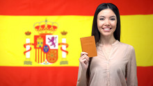 Smiling Asian Girl Holding Passport Against Spanish Flag Background, Citizenship