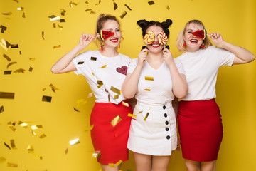 Group beautiful girl friend relaxing together posing with sweet colorful candy at yellow studio background. Happy smiling attractive woman having fun feeling rejoicing and happiness medium long shot