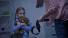 Mother With Belt Threatening Scared Daughter Hugging Teddy Bear Behind Window