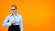Beautiful young woman in eyeglasses showing thumbs up on orange background