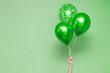 stylish birthday party or holidays with balloons. three green balloons on the green background with copy space for text. Hand  holding three bright colorful balloons indoor. greeting background