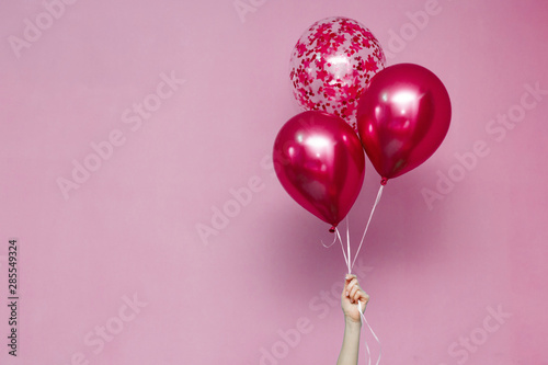 stylish birthday party or holidays with balloons.pink  balloons on the pink background with copy space for text.Hand  holding three bright colorful balloons indoor.