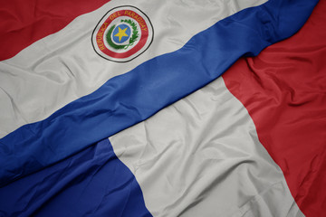 waving colorful flag of france and national flag of paraguay.