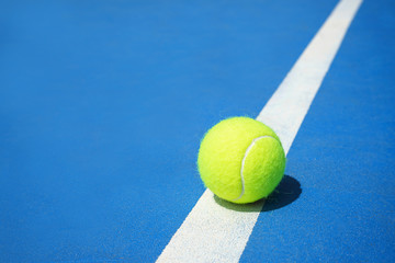 Wall Mural - Summer sport concept with tennis ball on white line on hard tennis court blue color.