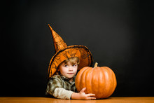 Happy Halloween. Cute Boy In Witch Hat Hugging Halloween Pumpkin. Jack O Lantern. Trick Or Treat. Halloween Party. Preparation For Halloween Holidays. Child With Pumpkin. Jack-o-lantern.