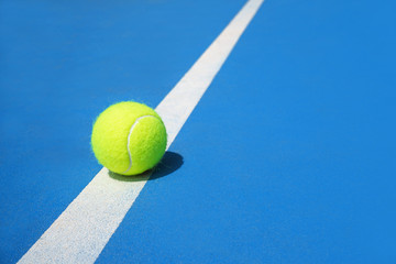 Wall Mural - Summer sport concept with tennis ball on white line on hard tennis court blue color.