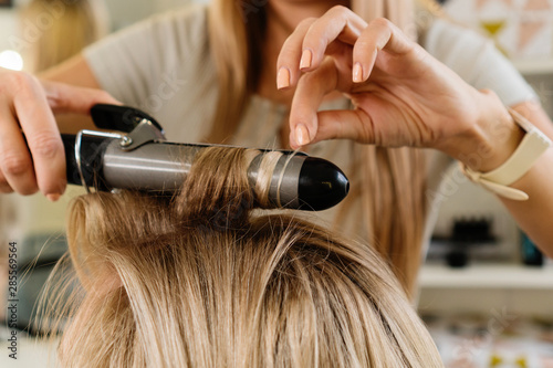 Hairstylist Using Curling Iron Of Female Client In Hairdressing