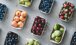 Summer fruit and berry assortment. Flat-lay of fresh strawberries, cherries, grapes, blueberries, pears, apricots, figs in eco-friendly boxes over grey background, top view. Local farmers produce