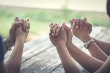 Group of people Praying Hands Over The Bible On Wooden Desk