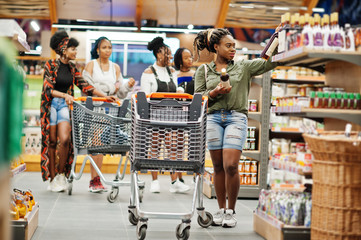 Poster - African woman choose wine at supermarket against her afro friends with shopping cart.