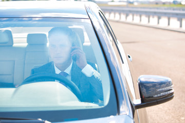 Wall Mural - Mature businessman talking on mobile phone while driving car