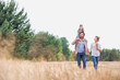 © MDBPIXS - Young Caucasian family walking across field with young child on her fathers shoulders with the wife holding a bouquet of flowers