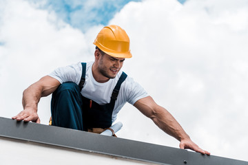 Wall Mural - handsome handyman in yellow helmet and uniform repairing roof