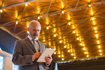 Wall Mural - Low angle view of confident senior businessman using digital tablet while standing against illuminated roof