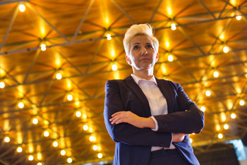 Wall Mural - Confident blond businesswoman standing with arms crossed against illuminated roof