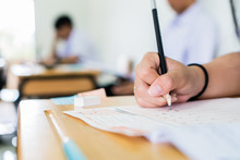 High School University Student Holding Pencil Writing Exam On Paper Answer Sheet, Writing Examination Room Doing Final Test In Classroom With Thai Uniform. Education Assessment Concept