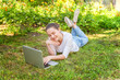 © Юлия Завалишина - Freelance business concept. Young woman lying on green grass lawn in city park working on laptop pc computer. Lifestyle authentic candid student girl studying outdoors. Mobile Office
