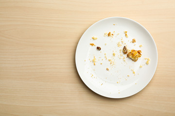 Dirty plate with food leftovers on wooden background, top view. Space for text