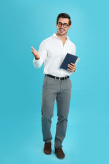 Wall Mural - Young male teacher with glasses and notebooks on light blue background