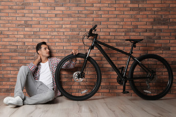 Wall Mural - Handsome young man with modern bicycle near brick wall indoors