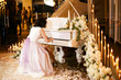 A girl in a beautiful dress plays the white piano during a wedding ceremony. Piano decorated with fresh flowers and vintage garland.