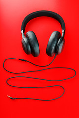 Wireless black headphones on a red background. View from above. In-ear headphones for playing games and listening to music tracks