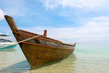 Naklejka na meble Old wooden boat and blue sea under cloudy sky on white beach in sunny day.