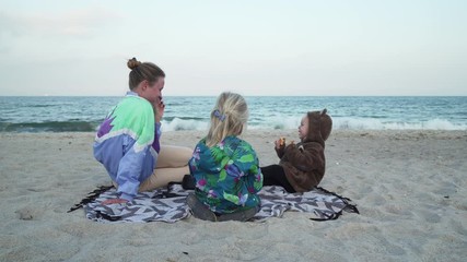 Wall Mural - Young beautiful family have a picnic at sandy sea shore at cloudy weather