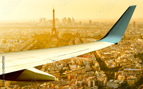 Plane flies above Paris in summer evening, France. Aerial panoramic view of Eiffel tower from airplane window. The plane\'s wing over streets of Paris at sunset. Flight and air travel to Paris.