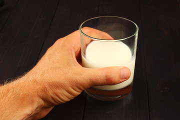 Wall Mural - glass of milk on a dark background in hand